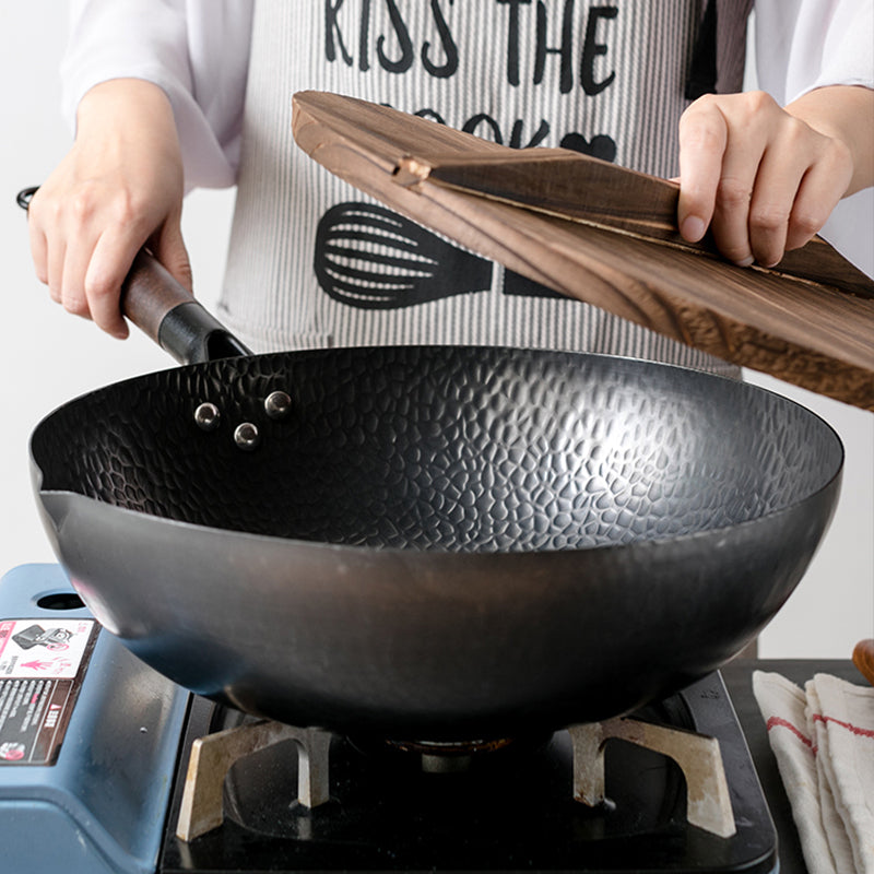 Wok en fonte sur le feu, couvercle en bois soulevé