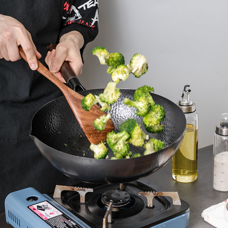 Wok en fonte avec sauté de brocolis sur un feu gaz