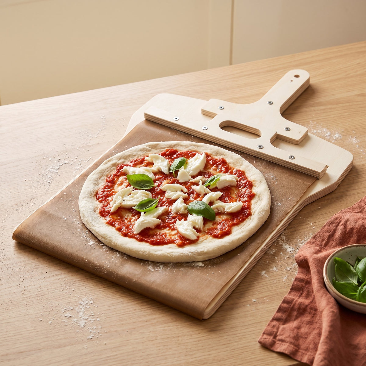 Pelle à pizza coulissante Fornello avec une pizza crue sur sa toile, sur un plan de travail en chêne