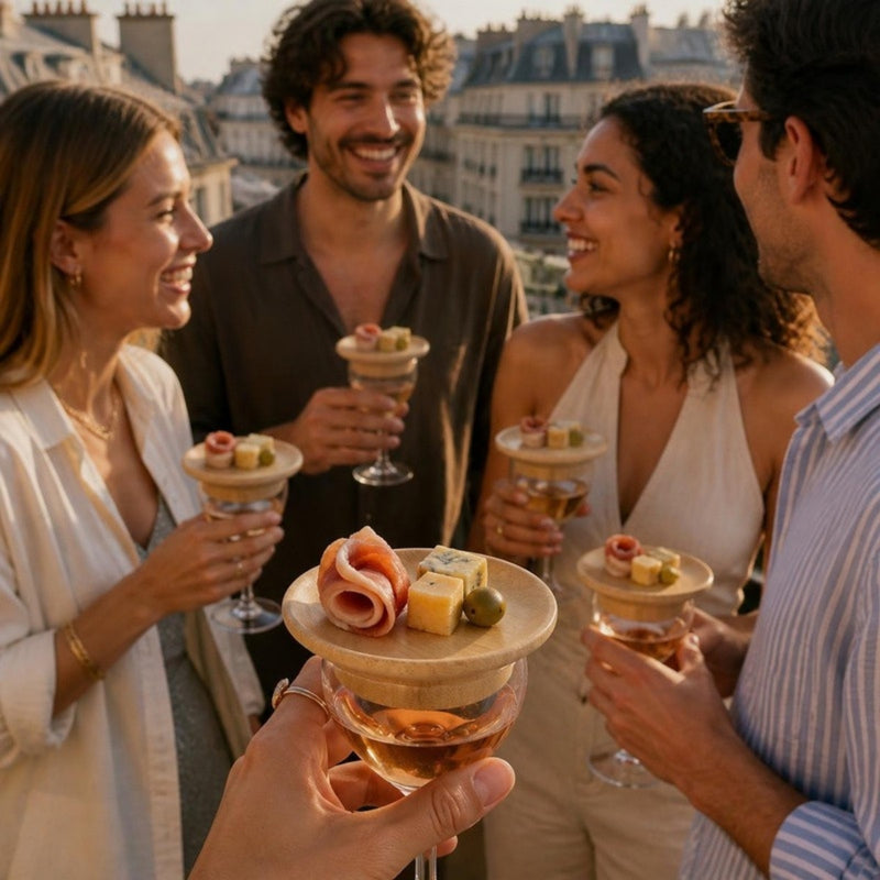 Amis à l'apéritif sur un balcon, verres coiffés de plateaux en bambou garnis