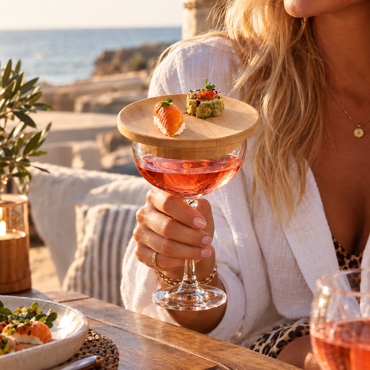 Femme tenant une coupe de rosé coiffée d'un plateau en bambou garni, au bord de la mer